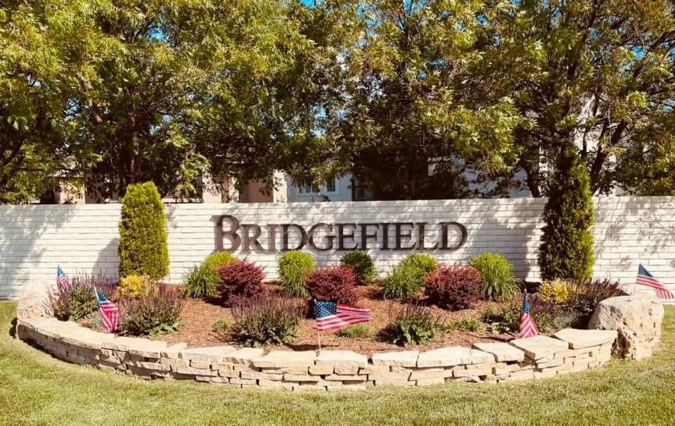 Bridgefield HOA entrance sign and welcome area with landscaping and American flags
